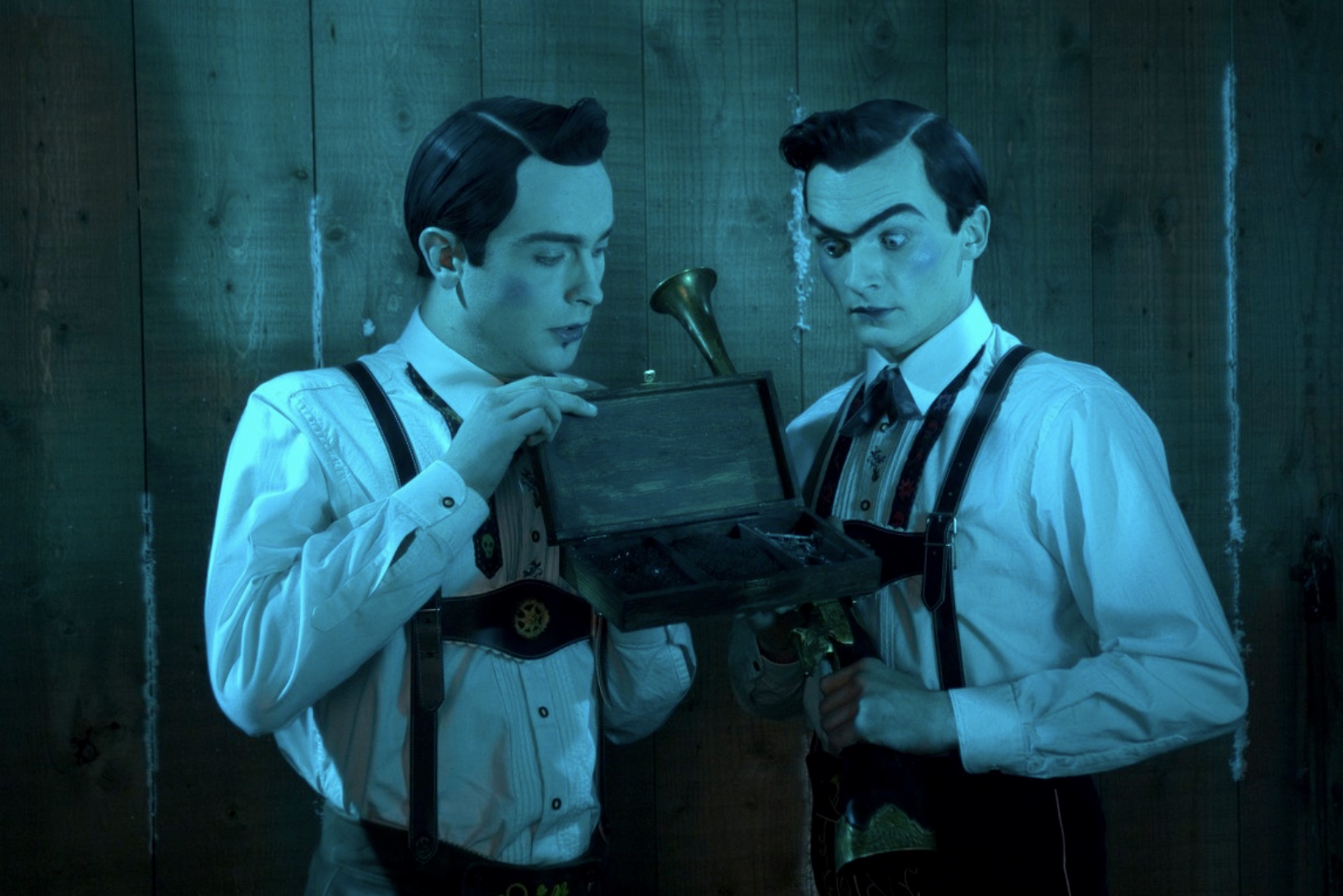 Two brothers look into a wood box while wearing lederhosen