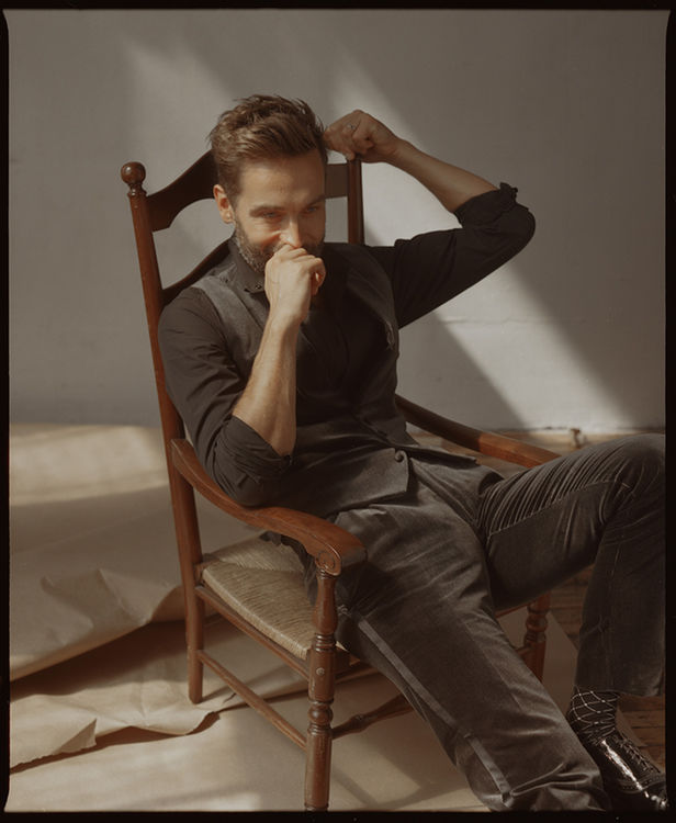 Tom is sprawled in a chair, dressed in velvet vest and trousers. Photo by Matthew Priestley.